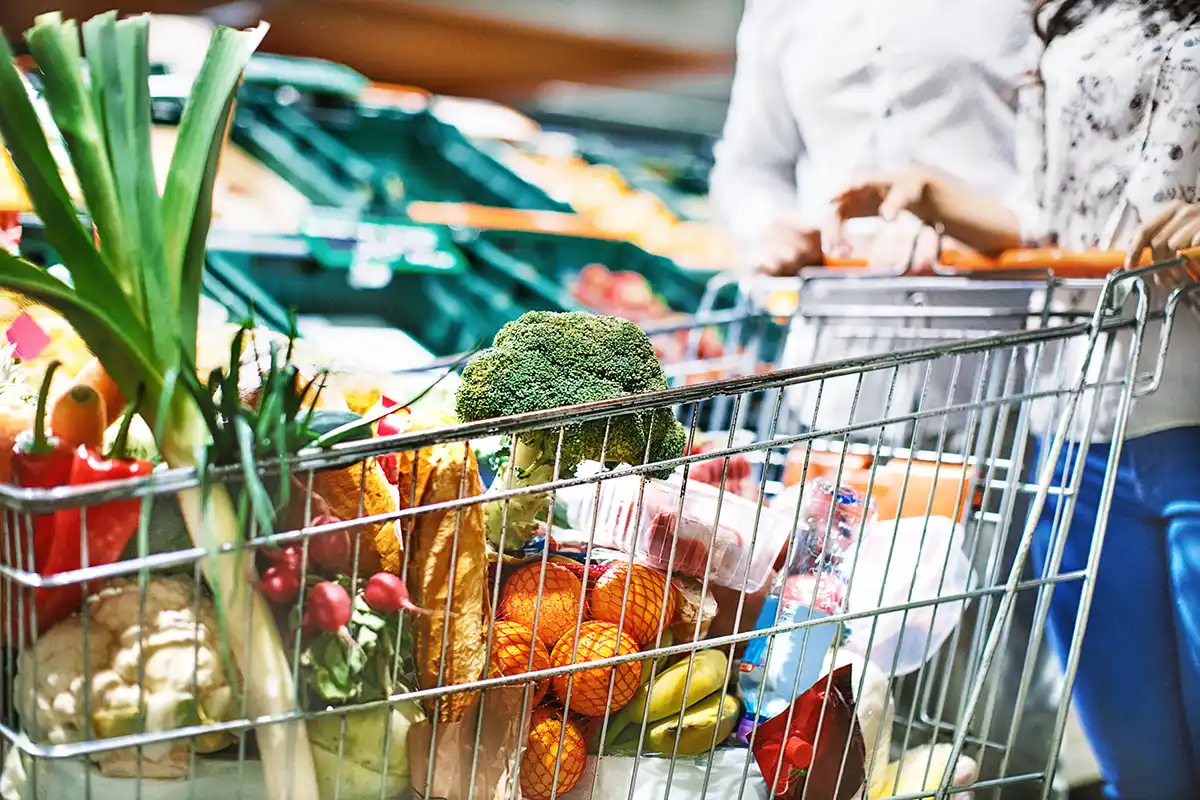 Shopping trolley filled with fresh groceries in a supermarket aisle.