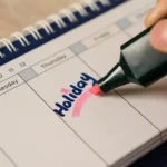 Person highlighting the word Holiday on a calendar with a pink marker.