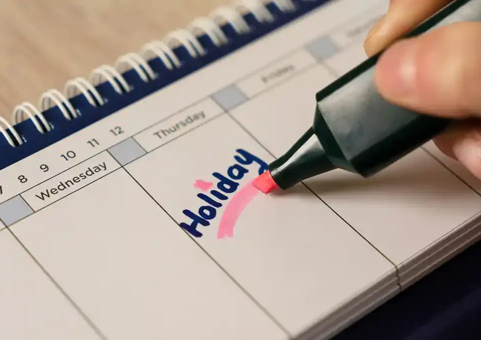 Person highlighting the word Holiday on a calendar with a pink marker.