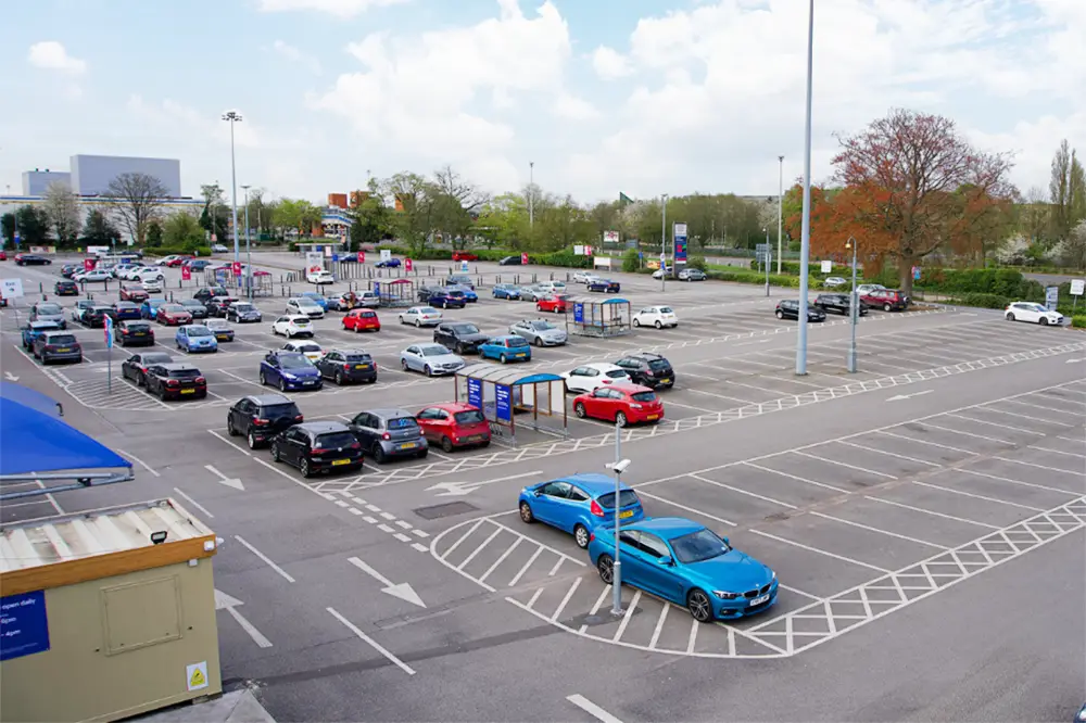 A busy supermarket car park with cars parked in marked bays and empty spaces.